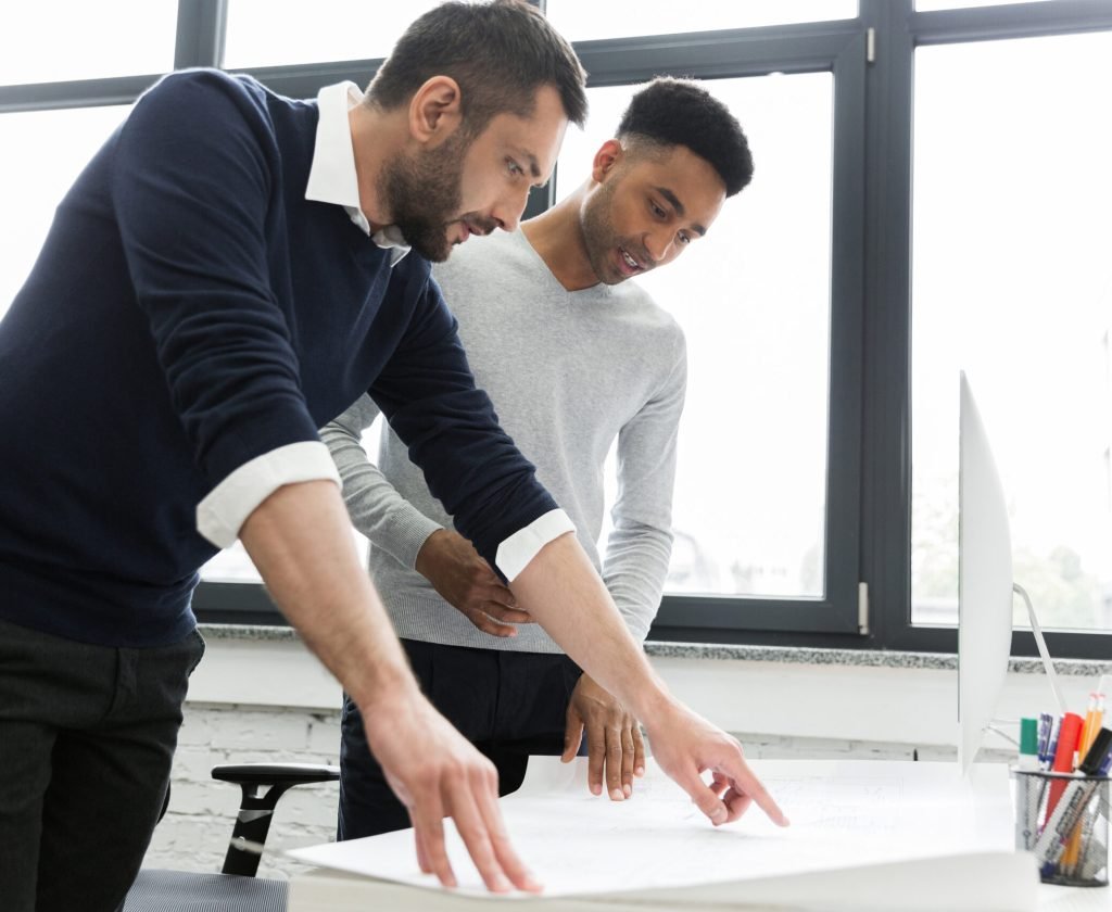 Two young male office workers pointing on a chart on a desk while standing